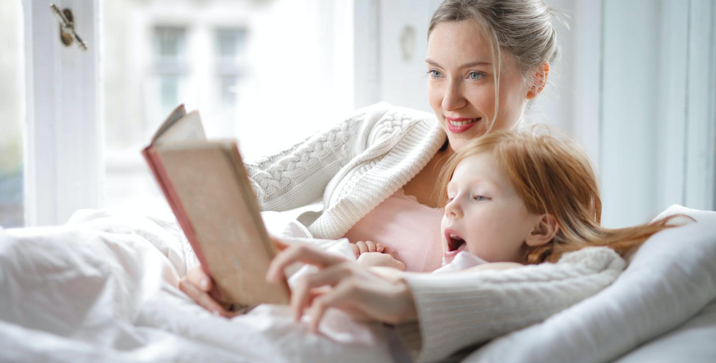 Mother reading story book to daughter at home