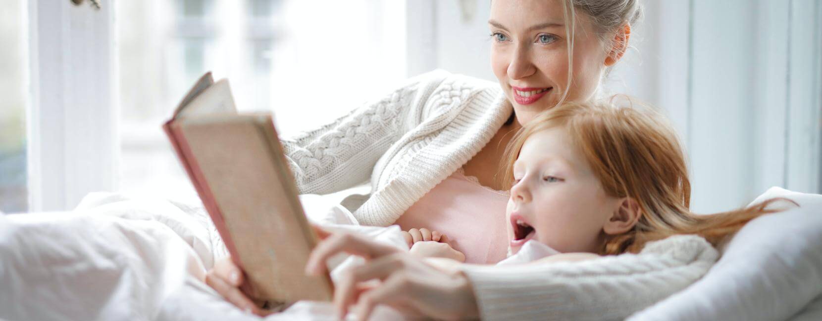 Mother reading story book to daughter at home