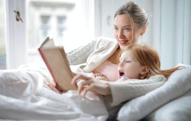 Mother reading story book to daughter at home